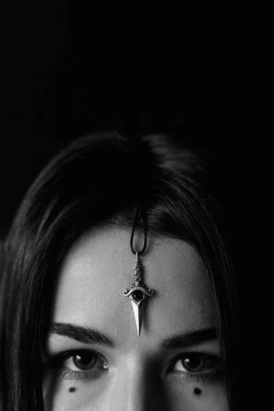 Close up of woman face with silver dagger pendant on her forehead