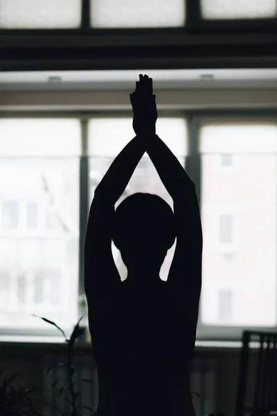 A silhouette of a woman doing yoga at home