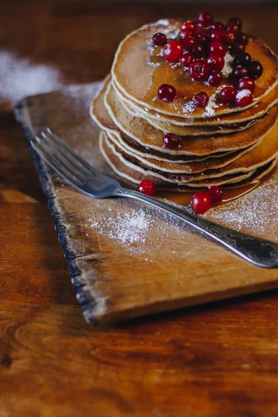 Stack of pancakes with cranberries and maple syrup on wooden board