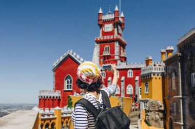 SINTRA, PORTUGAL - MAY 03, 2016: Young woman with backpack taking picture of old Pena National Palace in Sintra, Portugal clipart