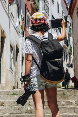 Young woman with backpack taking picture of old street with digital tablet in Lisbon, Portugal clipart