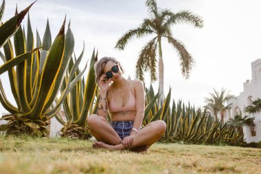 Güneş zevk yeşil çimenlerin üzerinde oturan seksi genç kadın