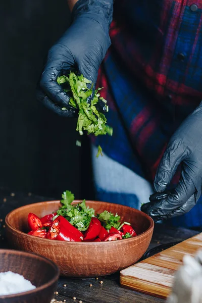 Donna mani in guanti neri mescolando peperoncino rosso piccante e prezzemolo — Foto Stock