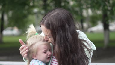 Annem küçük bir kızı yatıştırır. Annem küçük bir kızı yatıştırır. Anne kızını parkta bankta rahatlatıyor. Açık havada bahar olduğunu. Benim kızım ağlıyor, annem okşayarak ve onu öpüyor.