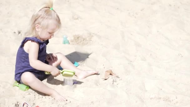 Маленька дівчинка на пляжі грає в іграшки для піску — стокове відео