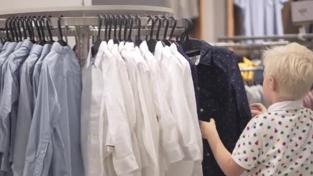 Jongen in een wit T-shirt in het winkelcentrum kiest een shirt — Stockvideo