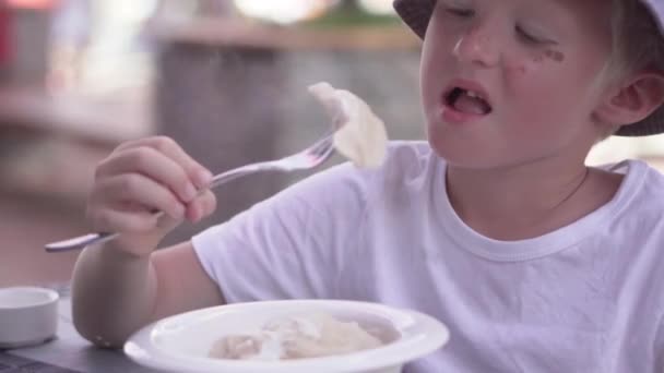 De jongen eet Varik aan een tafel in een café — Stockvideo