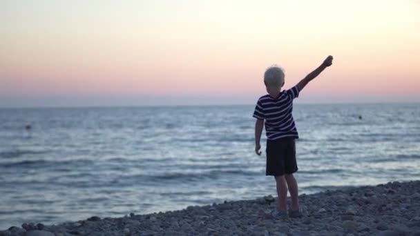 The boy throws stones at the sea at sunset — Stock Video