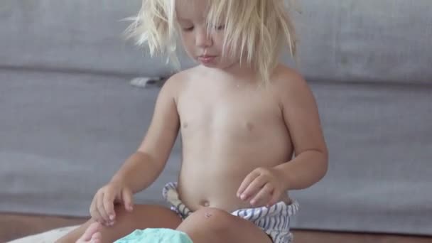 Liten flicka sitter på golvet och försöker sätta på en t-shirt — Stockvideo