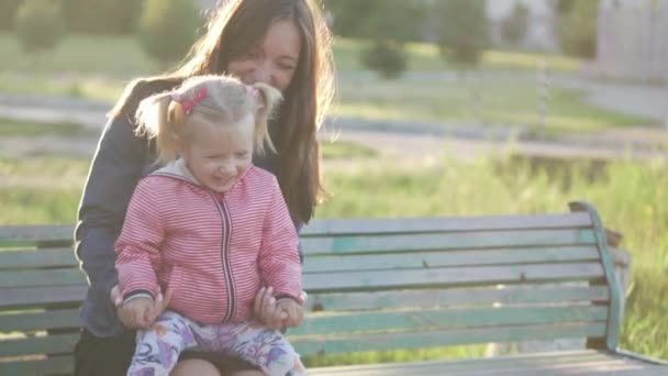 A mãe e a filha estão sentadas num banco do parque. Primavera é ao ar livre — Vídeo de Stock