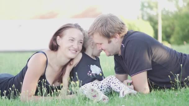 Dad, mom and little daughter are sitting on the green grass in the park — Stock Video