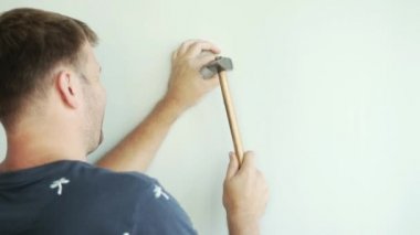 bir adam tarafından duvarın ayakta ve çekiçle çivi çekiç.