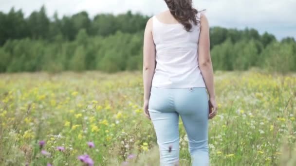 A menina está de pé com as costas para a câmera no campo com margaridas — Vídeo de Stock