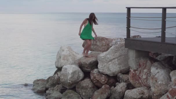 Una mujer está de pie sobre rocas cerca del mar — Vídeos de Stock