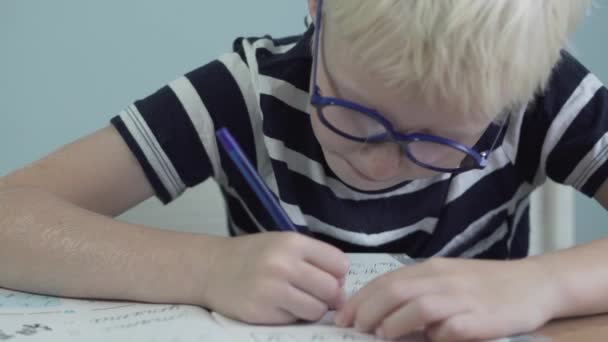 Un colegial con una camiseta a rayas hace su tarea — Vídeos de Stock