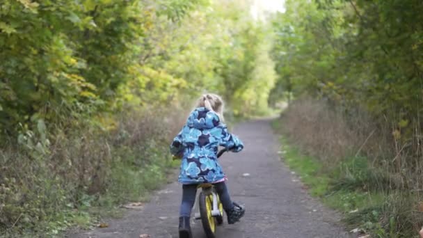 Ein kleines Mädchen reitet auf einem Waldweg — Stockvideo