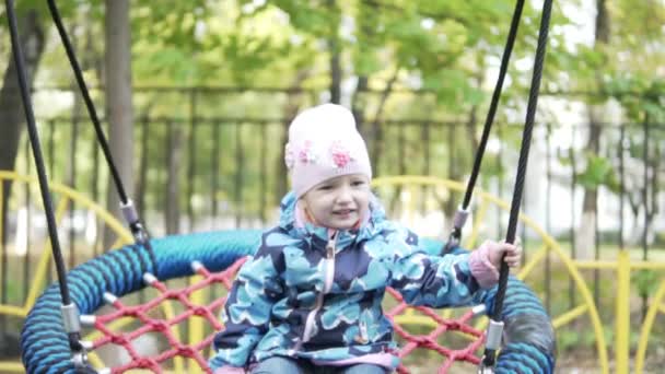 Чарівна маленька дівчинка катається на гойдалках на дитячому майданчику — стокове відео