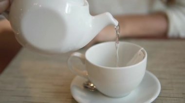 El üzerinde bardağı kaynar su ile beyaz bir su ısıtıcısı götürüyor