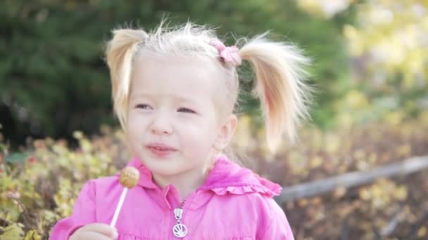 Kleines Mädchen saugt chupa chups draußen in den Park. — Stockvideo