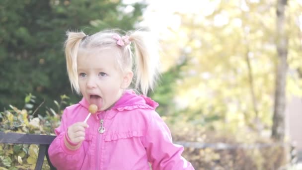Маленькая девочка сосёт чупа-чупы в парке. . — стоковое видео
