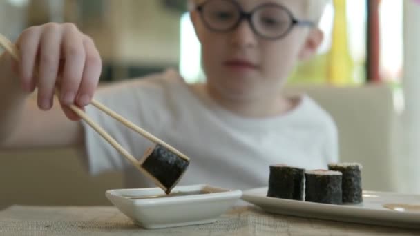 Een hongerig kind houdt Japanse stokjes met een rolletje. — Stockvideo