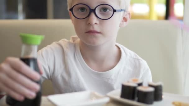 Um menino com óculos está sentado em uma mesa em um café — Vídeo de Stock
