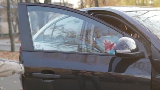 Blond chłopiec otwiera drzwi do czarnego auta i siedzi na siedzeniu w foteliku samochodowym. — Wideo stockowe