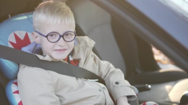 Pojken sitter i bilen i bilbarnstolen. Han spände. — Stockvideo