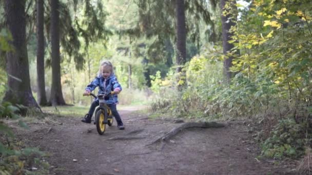 Маленькая девочка на велосипеде едет через осенний лес — стоковое видео