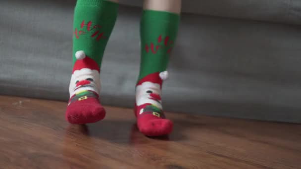 Dos piernas en calcetines de Navidad cuelgan del sofá — Vídeo de stock