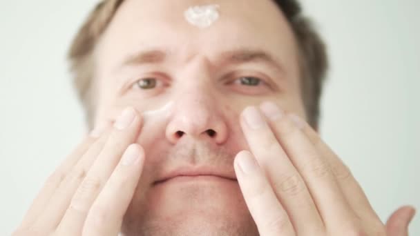 Hombre guapo aplica crema a la cara. — Vídeos de Stock