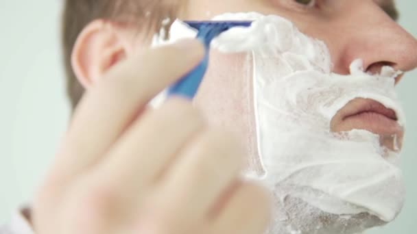 A man shaves his cheek with a blue razor. — Stock Video