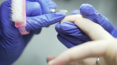 Donanım manikür çivi tedaviyle Close-up. Ana salonda bir manikür yapar. Eldivenli elleri, makine, fırça ve istemcinin elinde çerçevesinde