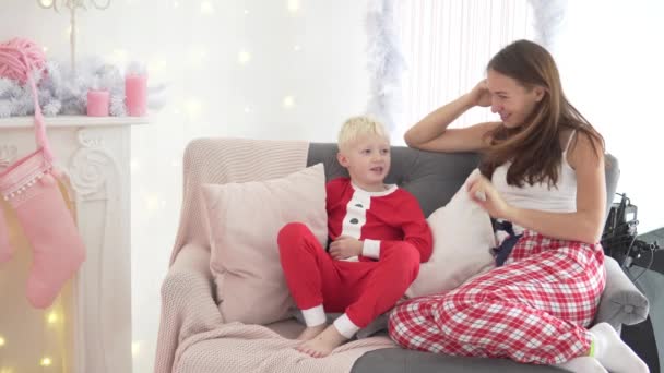 Mamá e hijo están sentados en el sofá junto al árbol de Navidad — Vídeos de Stock