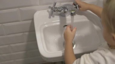 Küçük kız çocuk lavabolar eller için suda açar.