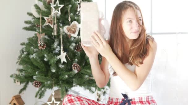 Una ragazza è seduta vicino alla finestra e sta considerando il suo regalo di Natale — Video Stock