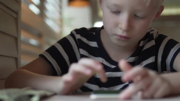 Un niño se sienta en una mesa en un café — Vídeos de Stock