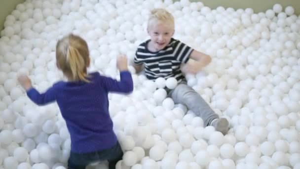 Bruder und Schwester spielen mit einem Pool mit weißen Bällen — Stockvideo