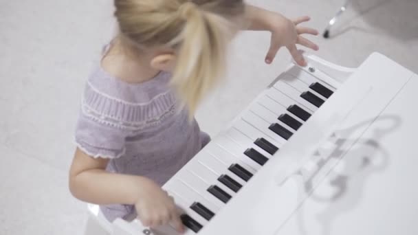 Una niña linda se sienta en un piano de niños con estilo y toca música — Vídeos de Stock