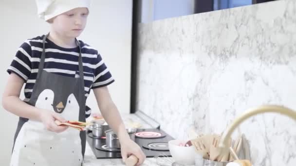 Красивый и веселый мальчик играет поваров в игрушечной кухне — стоковое видео