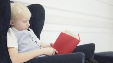 Yakışıklı sarışın çocuk bir koltukta oturur ve bir kitap okur