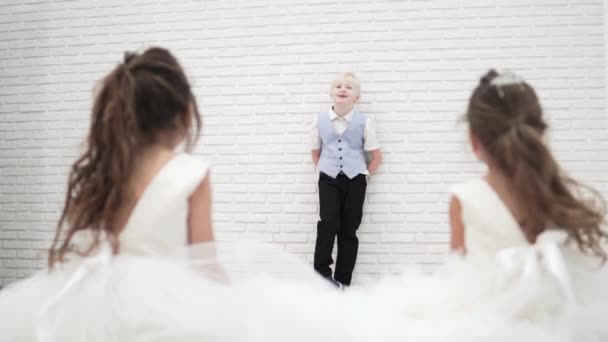 Ein hübscher blonder Junge steht an einer weißen Ziegelwand und erzählt etwas — Stockvideo