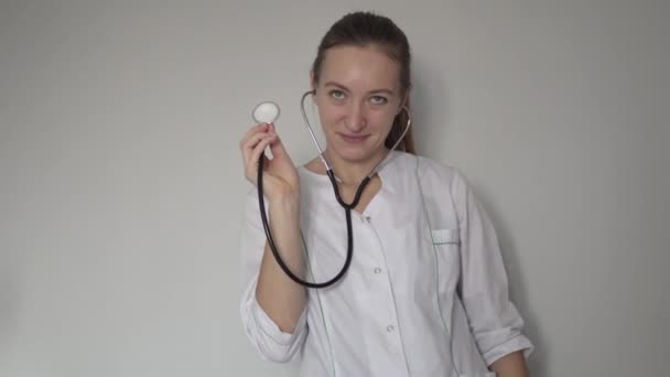 A beautiful woman in a doctor costume playfully leads a stethoscope — Stockvideo