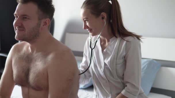Schöne Ärztin in weißem Mantel hört dem Stethoskop eines kranken Mannes zu. — Stockvideo