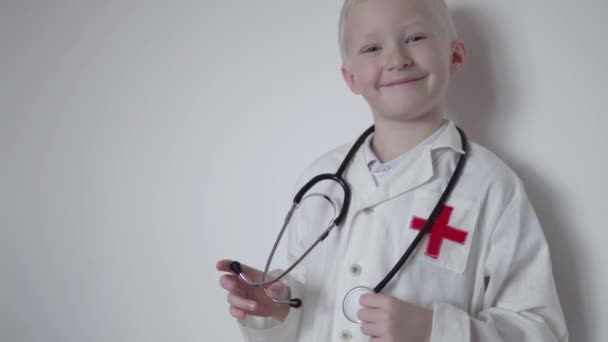 Menino louro bonito em um casaco médico branco sorri — Vídeo de Stock