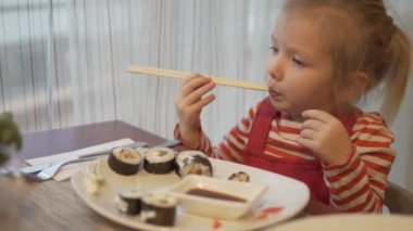 Küçük bir kız Suşi yiyor. O tahta çubukla roll bir parça alır