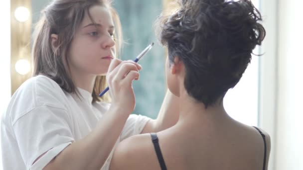 Jovem maquiador pinta um modelo elegante antes de fotografar — Vídeo de Stock