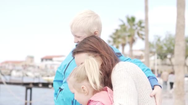 Мама с детьми смотрит на море. Дочь и сын обнимают женщину и улыбаются — стоковое видео