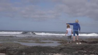 Küçük bir kız ve kardeşi deniz deki sahilde oynuyorlar.