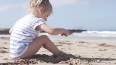 Deniz tarafından kumlu plajda oturan sevimli küçük kız.